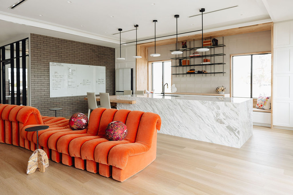 A linear pendant lights a kitchen island while round can lights provide ambient lighting and a linear cove light accentuates a textured wall in an office kitchen