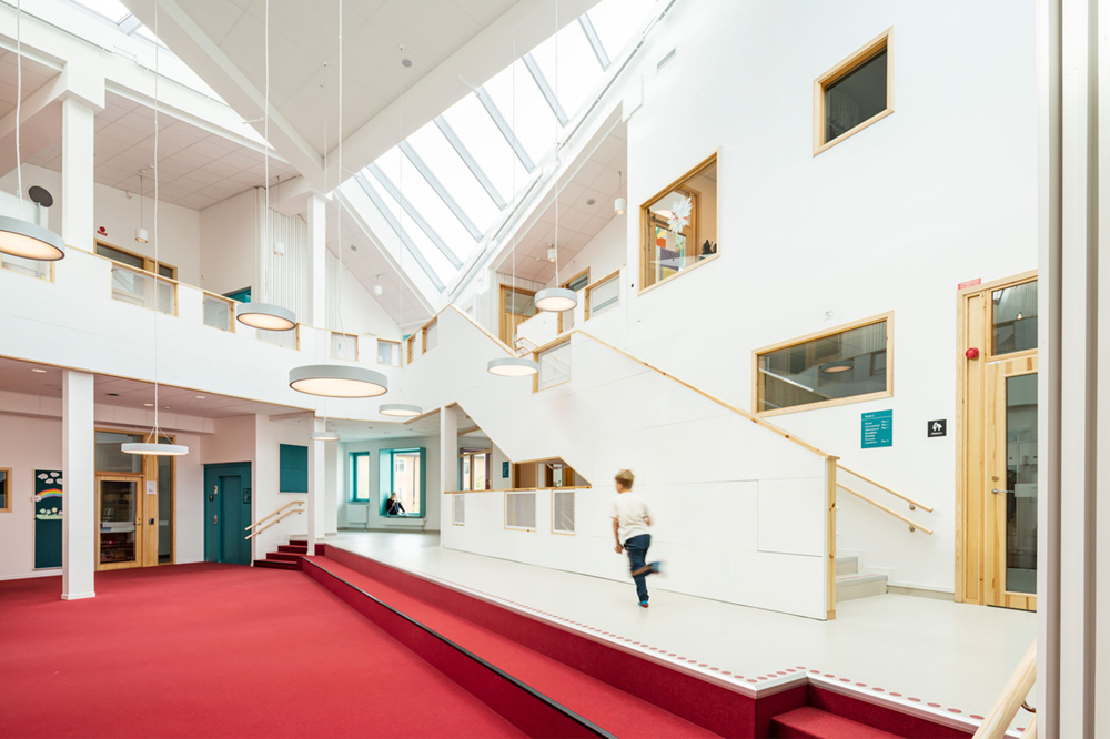 Suspended LED disk lights hang from a sloped vaulted ceiling at the Skälby School and Preschool in Stockholm, Sweden