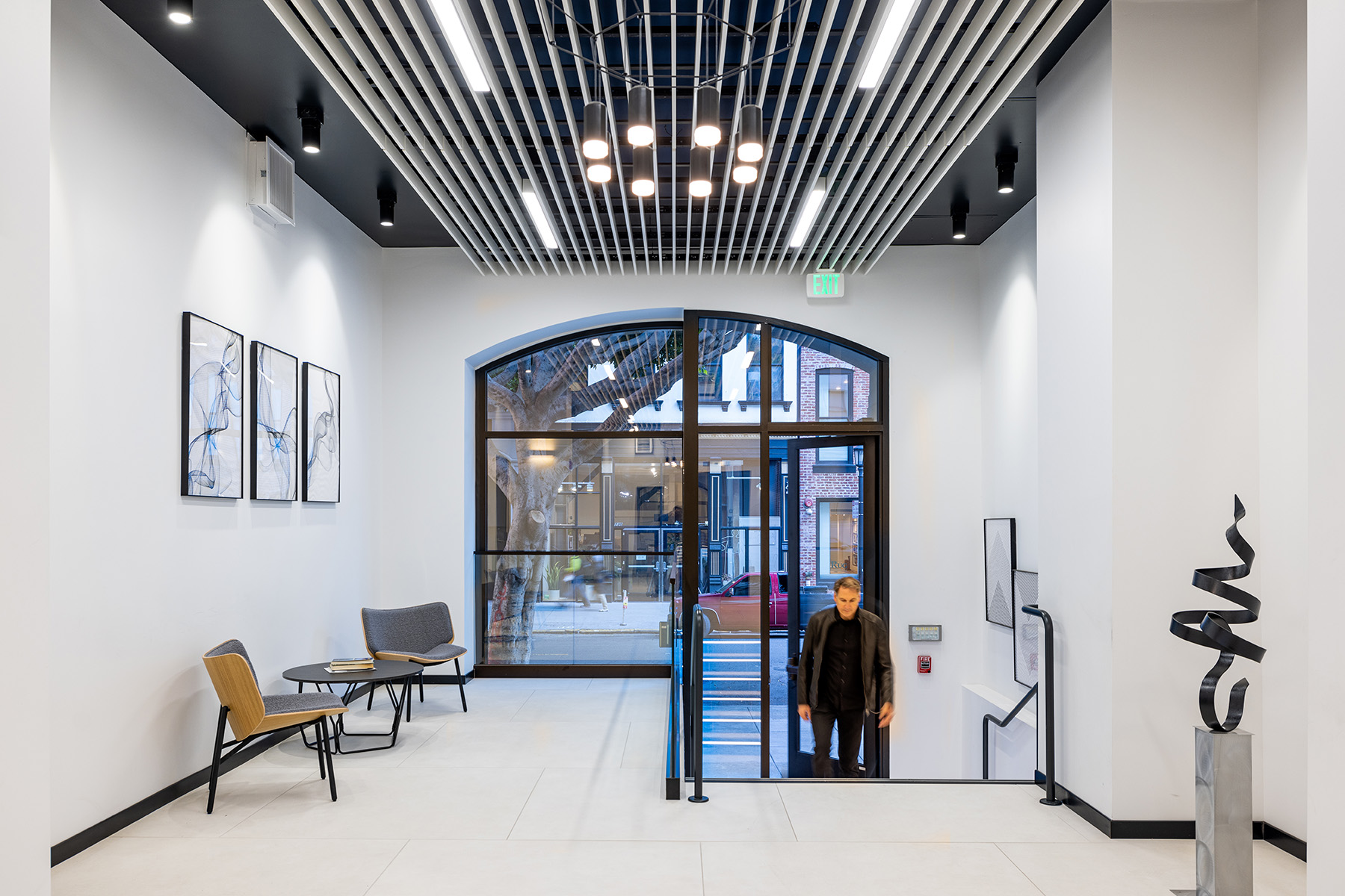 A combination of light fixtures including commercial pendant lights, linear recessed lights and cylinder downlights creates a play of light to highlight textures and surfaces throughout this office lobby.