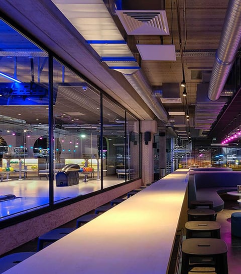 Cylinder downlights offer general illumination in a bowling alley lounge, while blue and magenta RBG lighting creates a fun atmosphere.