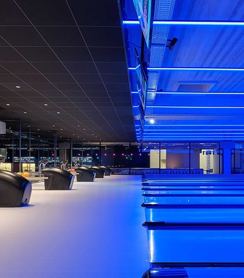 Linear recessed RGBW lighting in blue creates a cool atmosphere over the lanes of a bowling alley.