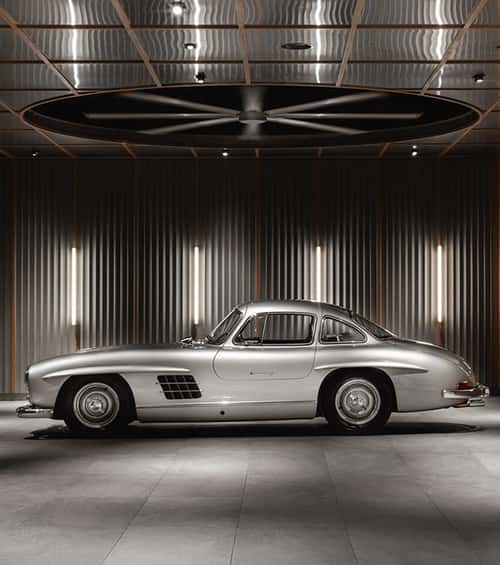 Vertical linear wall lights highlight textures on a showroom’s pleated, paneled wall, reflecting off the ceiling, adding functionality and style while illuminating a classic car.