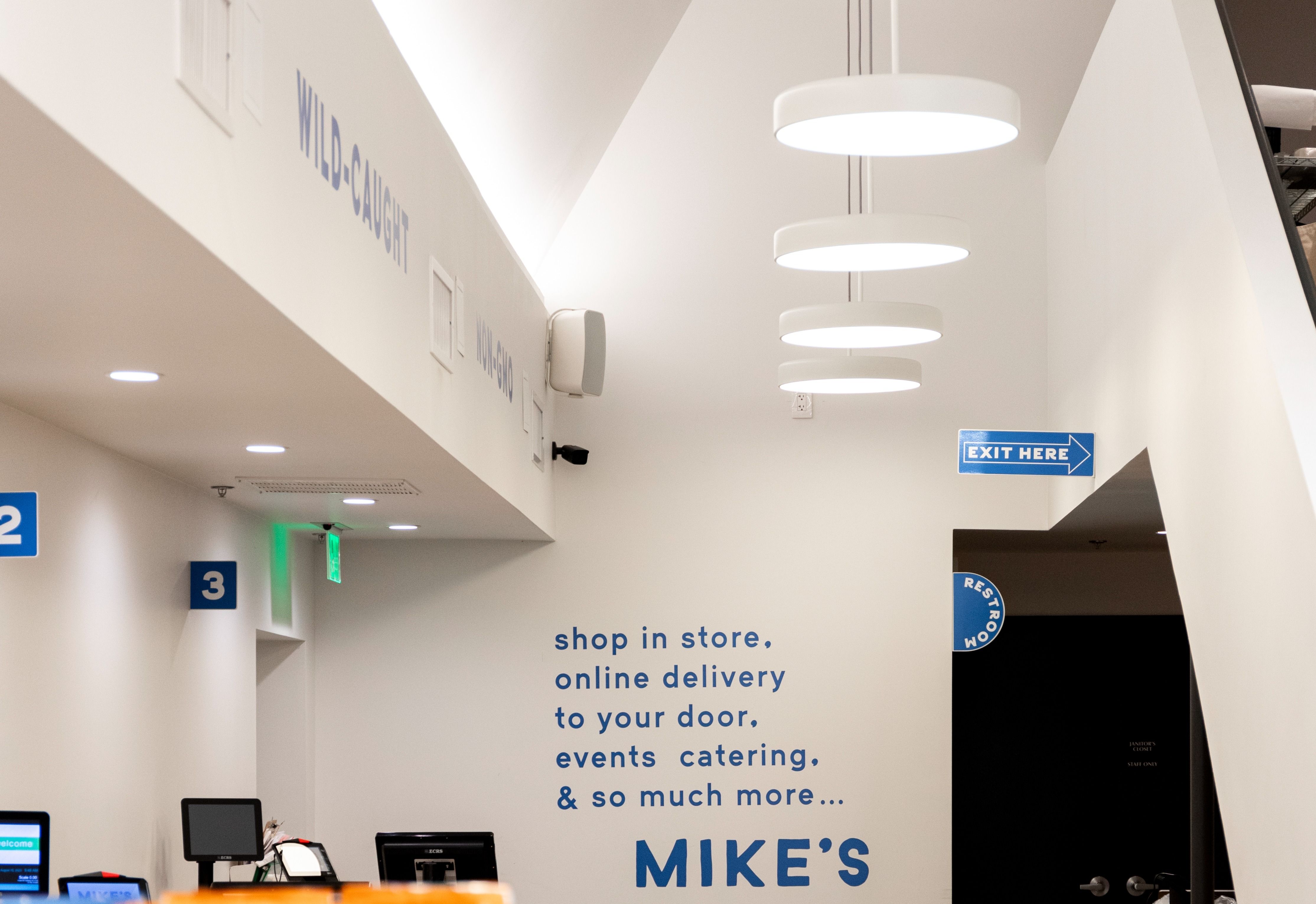 Flanged round recessed lights with neutral white (3000K) color temperature illuminate grocery store checkout counters while disk lights illuminate the path to the exit.