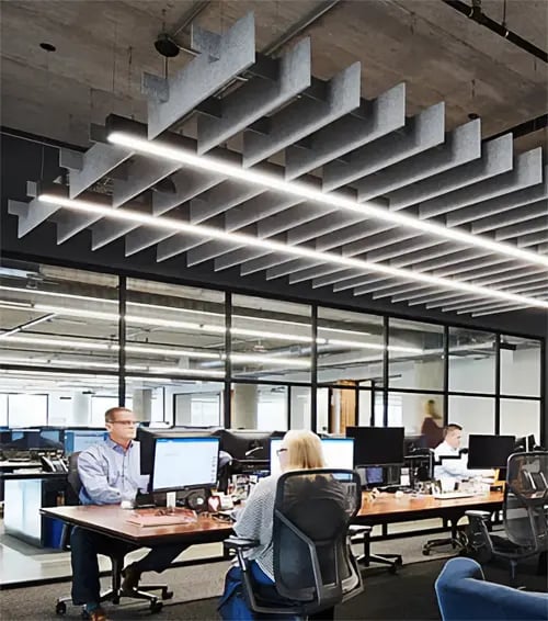 Acoustic linear pendant lighting suspended over an office conference room workspace with cylinder downlights over a common area