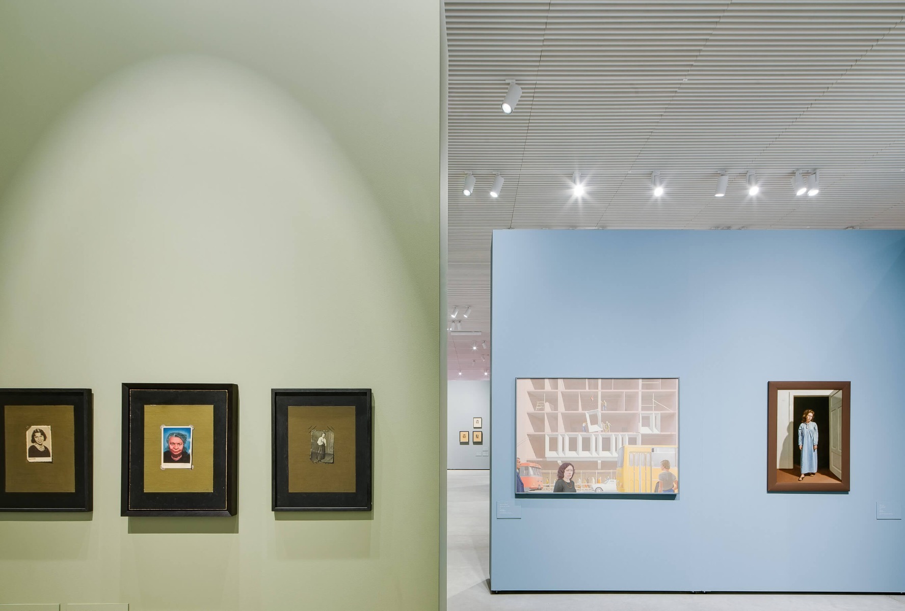 A track channel mounted in a wooden slat ceiling holds white LED track lights to illuminate wall art in a gallery. 